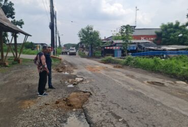 Teks foto : Kepala Desa Modong, H Masduqi, saat menunjukan kondisi jalan yang rusak dan berlobang.